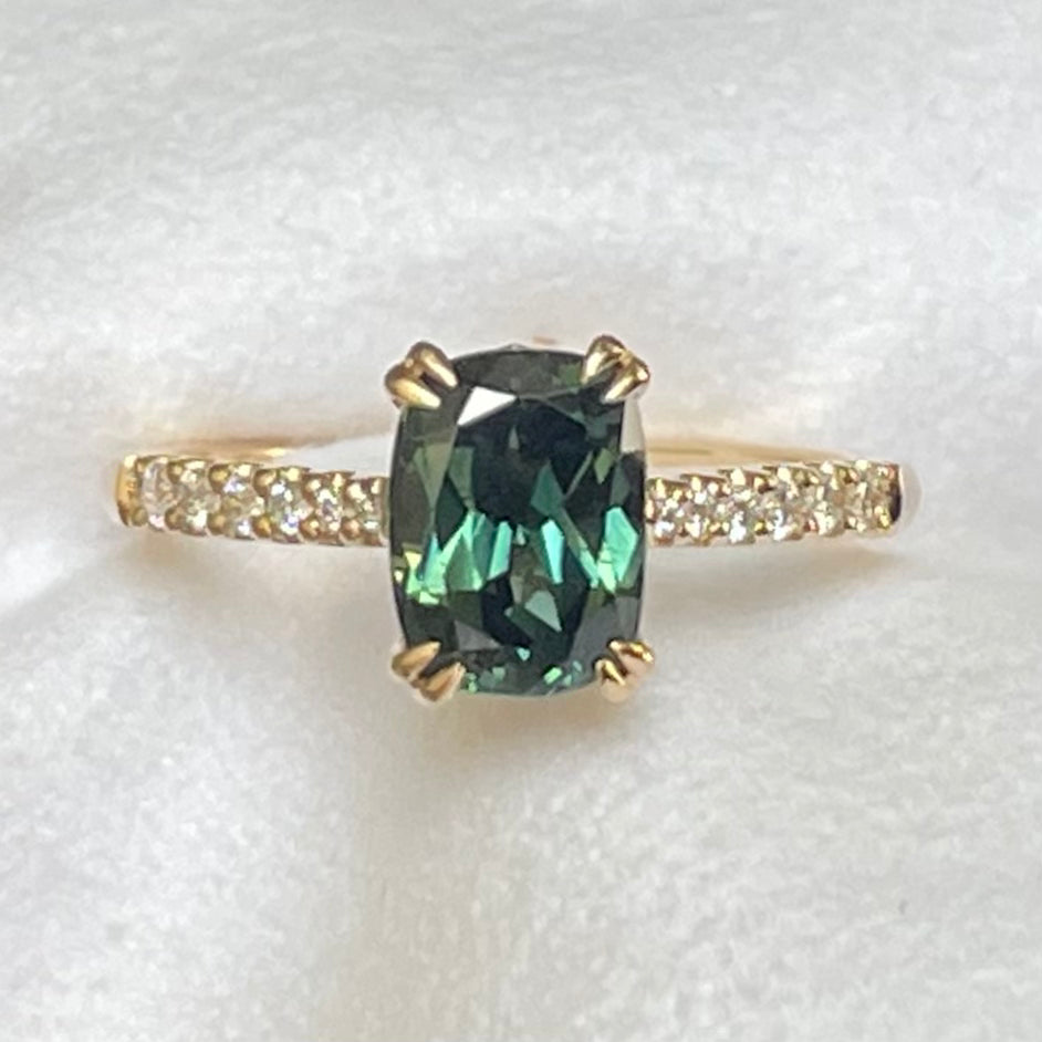 A Teal Green Australian Parti Sapphire from Rubyvale in QLD & is set with four double claws. The stone is beautifully complimented by 12 x Round Brilliant cut graduating diamonds total diamond weight 0.13pts and is set in 14ct Yellow gold.  The Sapphire measures 7.9 x 5.9mm & is 1.75ct   Available in Size M  Made with recycled metal in Sydney   Ethically sourced Gemstones